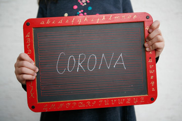Child holding Chalkboard with Corona lettering