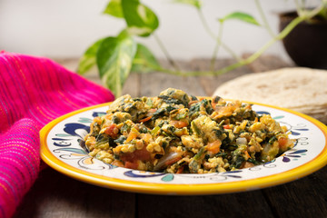 Mexican scrambled eggs with spinach on wooden background