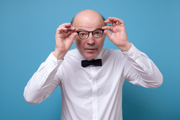 Naklejka premium Amazed senior man looking at camera through glasses having some doubts
