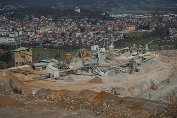 Detail of an open mine or quarry on a sunny day at Verd, Slovenia. Visible terraces and vast surface of sand and stones, with a city in the background.