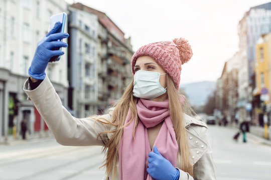 Woman with medical mask and gloves taking selfie in lockdown city