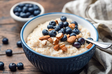 Oatmeal porridge with blueberries and almonds. Healthy breakfast porridge oats on a wooden table. Closeup view. Clean eating food - obrazy, fototapety, plakaty