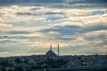 Skyline of Istanbul at sunset with silhouettes of mosques and old buildings in Suleymaniye district. Cityscape of Istanbul with passenger airplane over the ancient downtown in sun lights. 