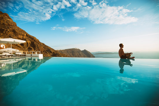 Man meditating balanced on the edge of an infinity pool overlooking a caldera view of view of the caldera on the Mediterranean Greek island of Santorini