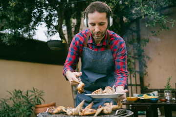Man cooking tasty wings on barbecue grill for outdoor lunch on beautiful summer day in a home garden