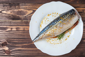 Pickled mackerel in a white plate. Raw unprepared fish. Traditional seafood delicacy, healthy eating concept. Against the background of a wooden tabletop