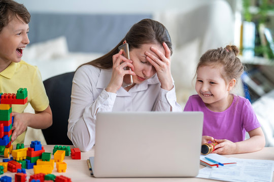Young women works at home with laptop, along with children. Children make noise