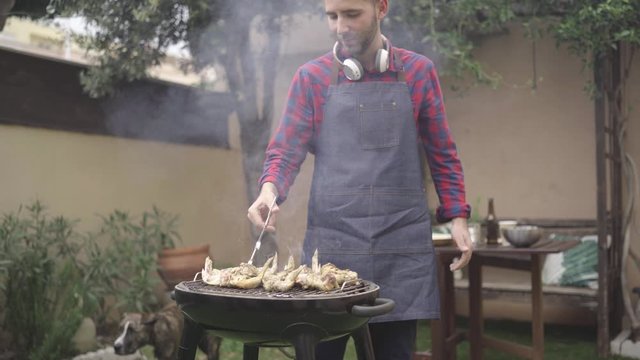 Man cooking tasty wings on barbecue grill for outdoor lunch on beautiful summer day in a home garden