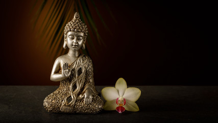 Old silver color statuette Buddha sitting in meditation pose with orhcid flower.