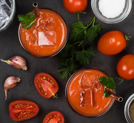 Tomato smoothie with parsley and ice in a glass on a dark background top view