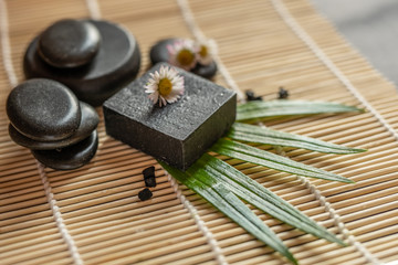 bar block of black carbon charcoal coal soap on a bamboo background with lava stones spa concept