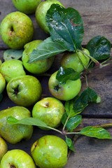 Top down view of freshly picked green apples with leaves on a wooden background.