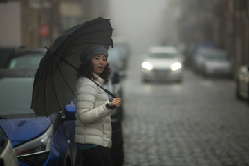 A mixed-race woman stands in the street in cloudy weather.