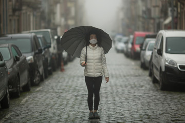 COVID-19, Coronovirus. Asian woman in antivirus mask stands in the middle of a deserted street in cloudy weather. Pandemic.