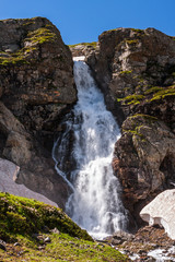 Fototapeta na wymiar Beautiful scenic landscape of Imeretinskiy waterfall in Caucasus mountains, Karachai-Cherkess Republic. Imeretinka river waterfall at summer in sunlight with splashes and blue sky.