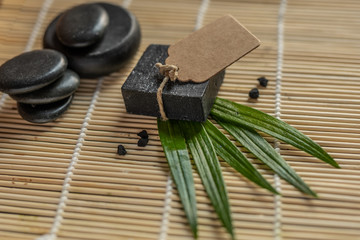 Obraz na płótnie Canvas charcoal coal carbon black soap bar on a raw wood bamboo background lava stone spa skin care hygiene concept 