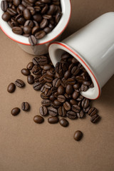 Two white porcelain cups with coffee beans. One cup is upset. View from above.