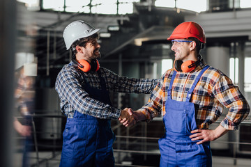 Two young builders in working uniform and helmets ready for a work, handshake.