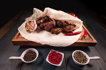 Appetizing fried meat lies on a wooden tray, among the seasonings. Studio photography of food in the cooking industry, dark background