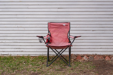 A collapsible red chair sits in front of a white wooden house