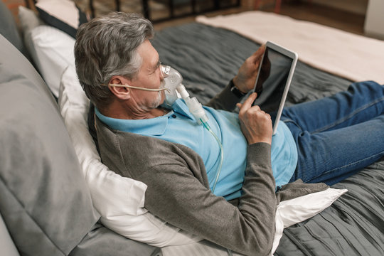 Man doing inhalation through oxygen mask at home bedroom and use his laptop