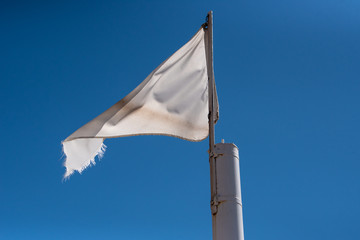 Tattered and dirty white flag with blue sky