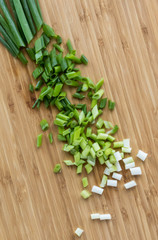 Top down close up view of green onion diced up on a wooden cutting board.