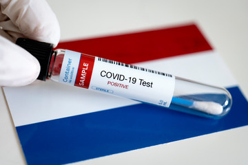 Obraz premium Testing for presence of coronavirus in Netherlands. Tube containing a swab sample that has tested positive for COVID-19. Dutch flag in the background.