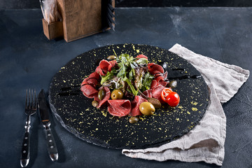 Beef carpaccio with arugula on a black plate, traditional Italian cuisine. Dark key, copy space,