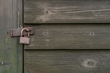 Large old padlock on a worn dark green wooden gate door.