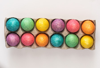 A dozen coloured easter eggs in a carton on white background