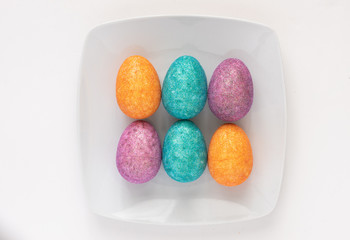 Six colourful Easter eggs on a white plate on white background