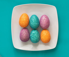 Six coloured Easter Eggs on a white plate on blue background