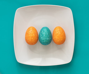 Three coloured Easter Eggs on a square plate on blue background
