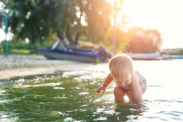 Cute adorable cheerful caucasian little blond toddler boy enjoy having fun playing at lake or river...