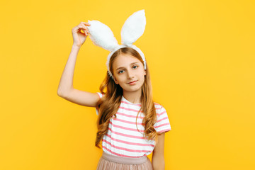 Happy little beautiful girl on her head with rabbit ears, posing on a yellow background