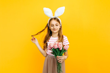 Happy beautiful girl on her head with rabbit ears, with a bouquet of tulips on a yellow background