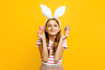 Beautiful happy girl on her head with rabbit ears and colorful Easter eggs in her hands, on a yellow background