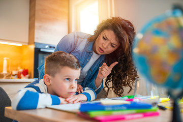 Obraz premium Photo of a young boy being homeschooled by his mother. The school has been closed during coronavirus outbreak and the classes have moved to e-learning platform.