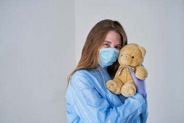 A close-up portrait of a doctor wearing an operating theatre outfit and brazing a teddy bear - isolated on a blue background. concept of tenderness and affection in medicine