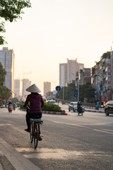 Women biking at sunset in Hanoi wearing rice hat 