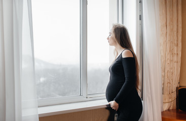 Fototapeta na wymiar A pregnant girl is breathing fresh air from the window