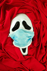abstract face of death in the form of a Halloween carnival mask with a medical protective mask on his face, the concept of protecting life from death, combating the pandemic, disease and pollution