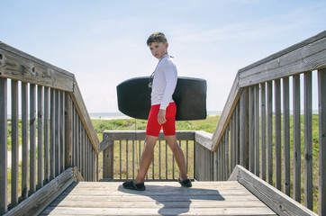 Male child with boogie board standing on wooden deck