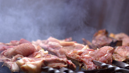  Flat pieces of pork with a strip of fat are fried on the grill. Smoke comes from hot coals