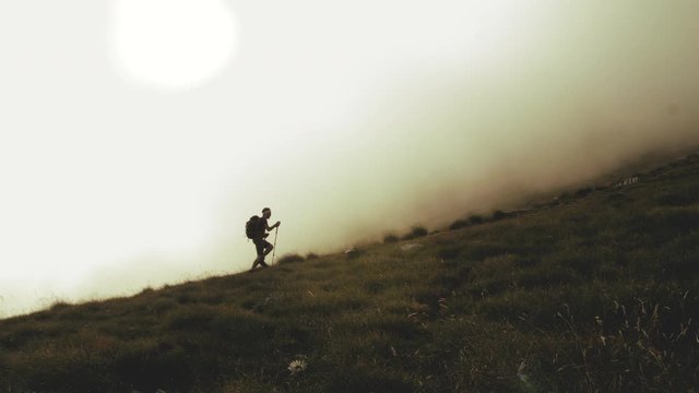 Young trekker man walking up the mountain in the fog with backpack, boots and trekking poles. Clouds and myst moving on the background. Abruzzo Italy.