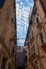 Antique buildings one in front the other with clothes hanging between them and sky in the middle with many small clouds 