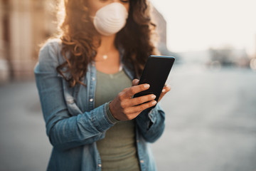 Young woman standing on empty city street and using phone. Healthcare, virus protection, allergy protection concept.