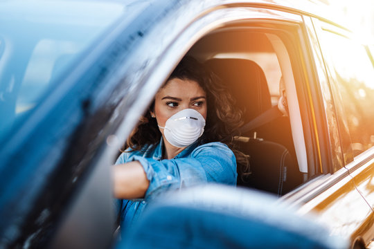 Young woman driving car with protective mask on her face.  Healthcare, virus protection, allergy protection concept.