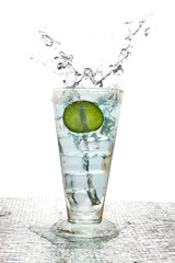 Half a lemon fell into a tall glass with ice inside. Until water splashes in a white background